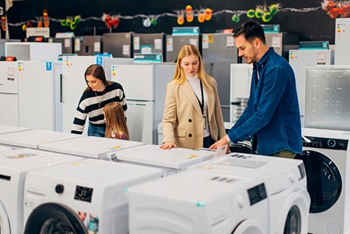 drie mensen staan in de winkel om wasmachines met elkaar te vergelijken
